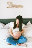 interior retrato do lindo jovem grávida mulher em repouso em cama foto