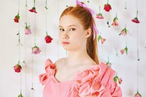estúdio retrato do bonita jovem Adolescência 15 - 16 ano velho ruivo menina vestindo Rosa coral vestir, posando em branco fundo com suspensão flores, beleza e moda conceito foto