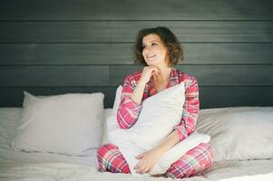cedo manhã retrato do feliz jovem grávida mulher em repouso dentro cama, vestindo acolhedor vermelho pijamas foto