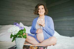 cedo manhã retrato do feliz jovem grávida mulher em repouso dentro cama, bebendo chá foto