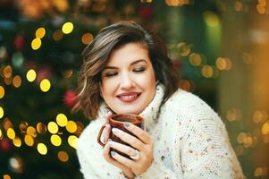 fechar acima retrato do feliz jovem mulher bebendo quente chocolate Próximo para Natal árvore foto