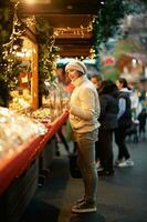 ao ar livre retrato do jovem mulher comprando doces às Natal mercado foto