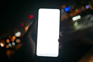 segurando inteligente telefone com esvaziar tela às noite foto