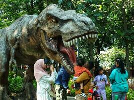 Bandung cidade, oeste Java, Indonésia. 19 Outubro 2023. realista modelo do dinossauro tiranossauro rex dentro Fora porta parque. família encontro com cheio do Diversão e felicidade foto