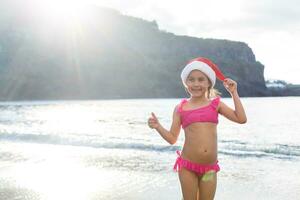 menina bonitinha de chapéu vermelho papai noel na praia foto