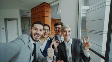pov do feliz o negócio equipe levando selfie retrato em Smartphone Câmera e posando para grupo foto durante encontro dentro moderno escritório dentro de casa