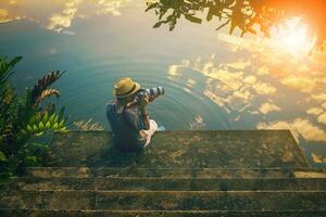 hipster homem levando uma fotografia em cais contra lindo céu refletir em lago foto