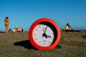 uma vermelho relógio em a de praia com pessoas dentro a fundo foto