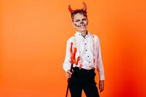 menino diabo em pé meia-volta contra um fundo laranja em maquiagem de baile de máscaras. conceito de halloween foto