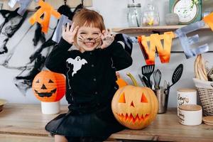 menina engraçada sentada ao lado da abóbora e mostrando um gesto assustador. - conceito de halloween foto