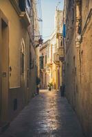 pequeno limitar rua em Malta com antigo edifícios dentro brilhante Sol raios foto