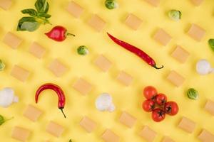 macarrão, pimentão, manjericão, tomate em um fundo amarelo. foto
