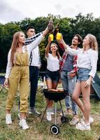 uma companhia de amigos levantando uma garrafa com uma cerveja no acampamento. - imagem vertical foto