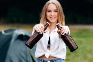 mulher em pé e segurando uma cerveja no acampamento. retrato de close foto