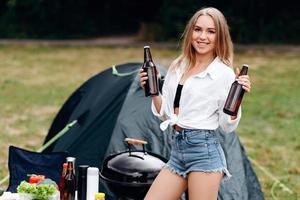 mulher em pé segurando uma cerveja no acampamento foto