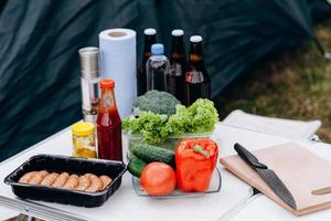 cerveja, salsichas e legumes frescos na mesa ao ar livre foto