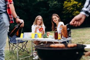 mulheres sorridentes sentadas à mesa com comida fresca e olhando para a churrasqueira foto