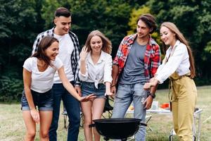 uma companhia de amigos se divertem no acampamento em pé ao lado do churrasco foto