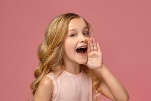 pequeno menina com uma loiro encaracolado cabelo, dentro uma Rosa vestir é posando para a Câmera foto