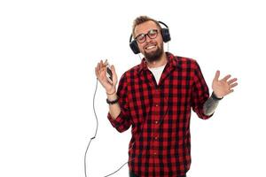 jovem hipster homem dentro xadrez camisa e óculos vestindo fones de ouvido olhando feliz em branco fundo. foto