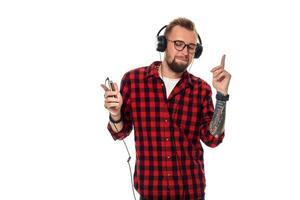 jovem hipster homem dentro xadrez camisa e óculos vestindo fones de ouvido olhando feliz em branco fundo. foto