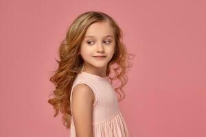 pequeno menina com uma loiro encaracolado cabelo, dentro uma Rosa vestir é posando para a Câmera foto