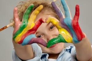 lindo pequeno menina com uma pintado mãos é posando em uma cinzento fundo. foto