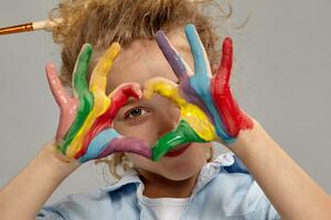 lindo pequeno menina com uma pintado mãos é posando em uma cinzento fundo. foto