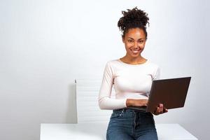 garota alegre descansando em pé no escritório segurando um laptop foto