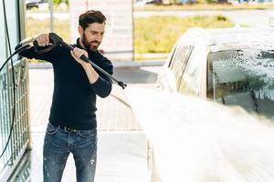 visão horizontal do homem caucasiano limpando seu automóvel com água pressurizada Oi na rua durante o verão. carro lavando por seu conceito de dono do sexo masculino foto