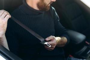 conceito de condução segura. jovem positivo apertando o cinto de segurança do carro, vista lateral, copie o espaço. caucasiano alegre começando uma viagem de carro, alugando um carro aconchegante e agradável para viajar foto