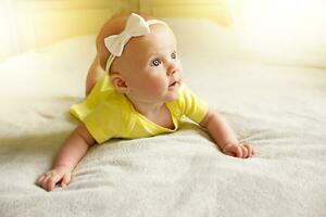 bonitinho, doce e encantador pequeno menina dentro uma amarelo maiô deitado em a cama e sorridente. a conceito do uma saudável bebê foto