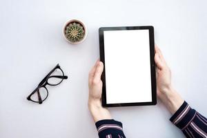 mesa de escritório branco de vista superior com óculos e cacto. um tablet em mãos masculinas foto