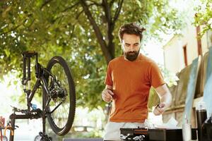 dedicada em forma e ativo homem lado de fora demonstrando comprometimento para mudando e protegendo bicicleta componentes para verão ciclismo lazer. cenário do jovem caucasiano masculino arranjo profissional equipamento foto