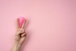 copo menstrual rosa no braço feminino isolado em um fundo rosa. dias críticos de conceito foto