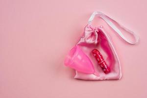 copo menstrual rosa e tampão deitado sobre um saco de seda isolado em um fundo rosa. dias críticos de conceito foto