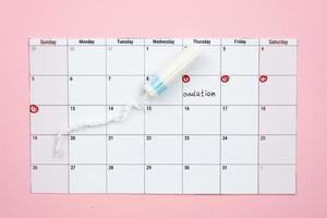 calendário menstrual e tampão de mulher deitada sobre fundo rosa. - imagem foto