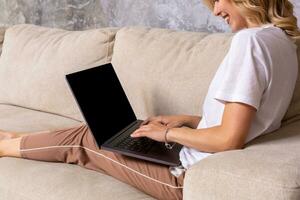 mulher em sofá trabalhando em computador portátil com brincar em branco tela. esvaziar cópia de espaço em monitor para anúncio. Preto tela. foto