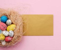 ovos de páscoa no ninho e cartão de felicitações no fundo rosa foto