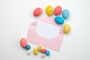 ovos de páscoa lindamente coloridos e um lindo envelope em branco em um fundo branco foto