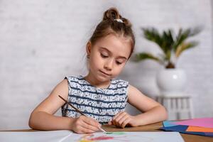 inspirado pequeno menina às a mesa desenhar com tintas foto