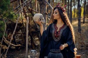 bruxa dentro preto, grandes vestir, com vermelho coroa dentro dela longo, encaracolado cabelo. posando dentro pinho floresta. segurando crânio. feitiços, Magia e feitiçaria. fechar-se. foto