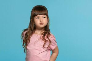 lindo pequeno menina vestindo dentro uma Rosa camiseta é posando contra uma azul estúdio fundo. foto