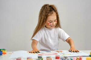 pequeno menina dentro branco camiseta sentado às mesa com que homem e tintas em isto, posando com pintado face e mãos. isolado em branco. médio fechar-se. foto