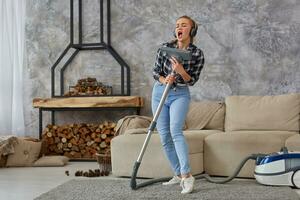 alegre jovem mulher desfrutando só cantando com vácuo limpador enquanto limpeza casa foto