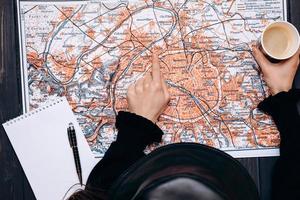 vista superior de uma donzela apontando para um mapa com um café na mão. conceito de planejamento de viagens foto