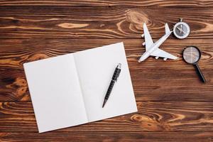 em uma superfície de madeira, uma folha de papel em branco e uma caneta, um avião e uma bússola, conceito de viagem foto
