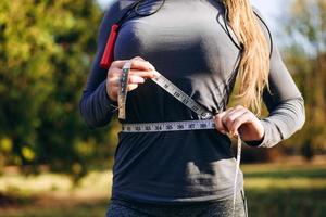 mulher atlética e magra medindo a cintura com fita métrica após treino ao ar livre foto