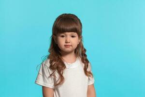 lindo pequeno menina vestindo dentro uma branco camiseta é posando contra uma azul estúdio fundo. foto