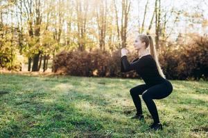 garota esbelta fazendo agachamento enquanto se exercita ao ar livre foto